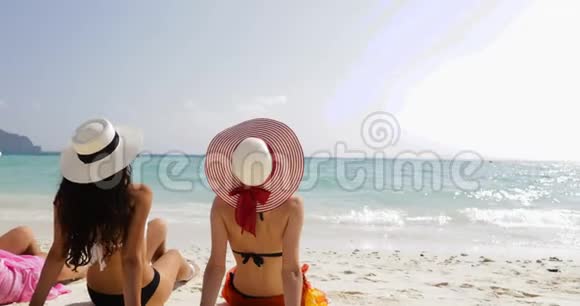 后景三个穿比基尼和草帽的女孩在海滩上享受日光浴女游客在暑假视频的预览图
