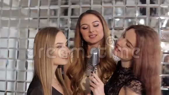 三个漂亮的女孩在卡拉OK酒吧里用麦克风唱歌视频的预览图