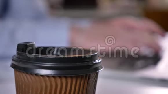 办公室里的一杯咖啡摆在桌子上商人的手在背景上用笔记本电脑打字背景模糊工作视频的预览图