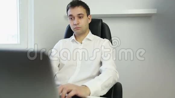 年轻的商人在笔记本电脑上完成打字然后躺在办公椅上视频的预览图