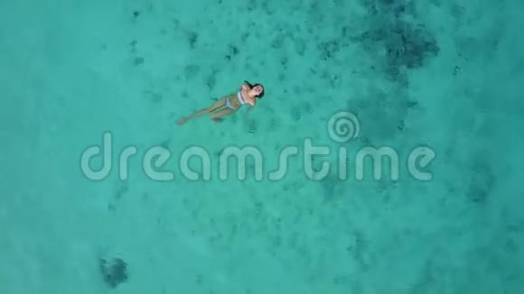 一个迷人的女人穿着比基尼漂浮在清澈的大海上的空中景色印度洋游泳的漂亮姑娘视频的预览图