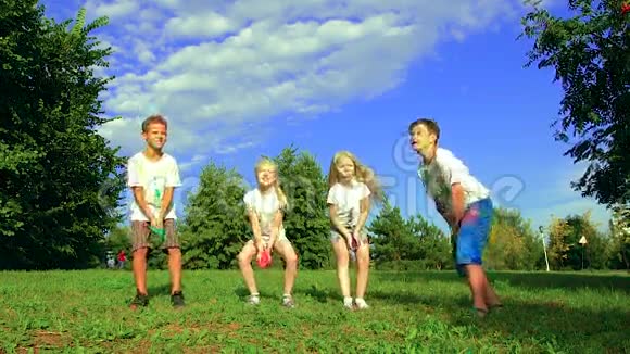 四个孩子组两个男孩和两个女孩在绿色草地上享受阳光明媚的一天并向空中投掷圣粉视频的预览图