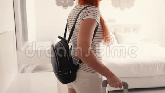 年轻快乐的女人带着手提箱进入她的酒店房间视频的预览图