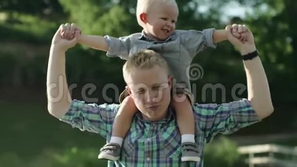 快乐的年轻父亲把儿子背在肩上抬起来小男孩背着背坐着视频的预览图