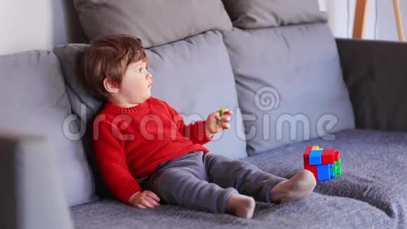 穿着红色毛衣坐在沙发上的滑稽小男孩视频的预览图