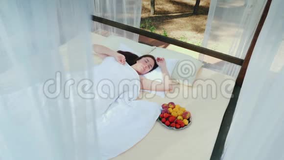 一个年轻的女人在一个休息室醒来窗帘覆盖着在她附近有一盘水果华丽的浪漫假期视频的预览图