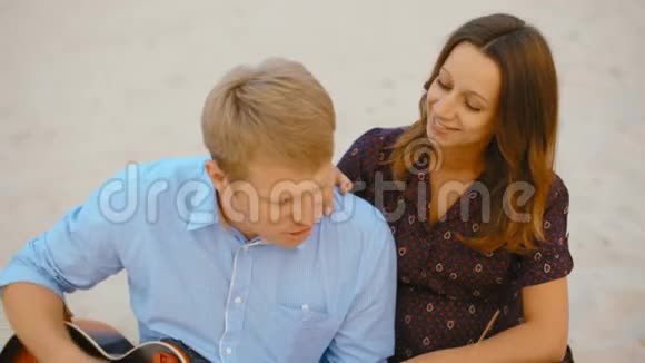 年轻夫妇正坐在沙滩上弹吉他唱歌微笑视频的预览图