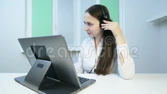 戴着耳机的漂亮女孩在笔记本电脑上的摄像机上讲话视频的预览图