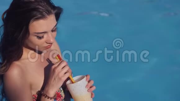 坐在泳池边喝鸡尾酒的漂亮年轻女人视频的预览图