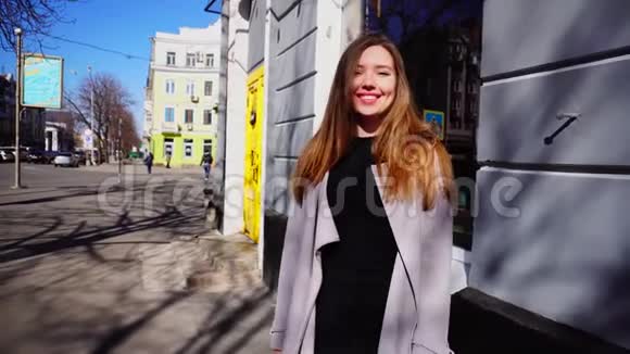 微笑的女孩穿着灰色外套和黑色连衣裙在城市里散步视频的预览图