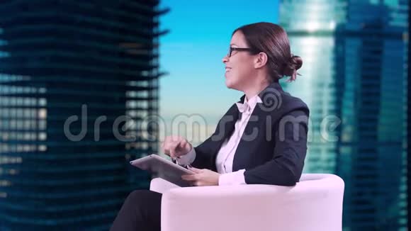 电视演播室戴眼镜的深色头发她穿着西装坐在工作室里接受采访视频的预览图