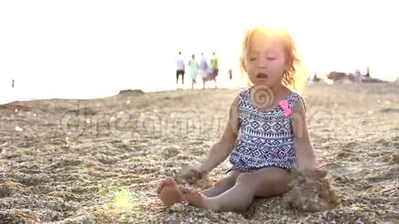一个小女孩坐在海滩上笑着扔沙子的慢动作视频的预览图