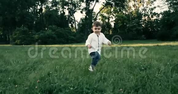 可爱的小男孩穿着白衬衫在草地上奔跑动作缓慢4k视频的预览图
