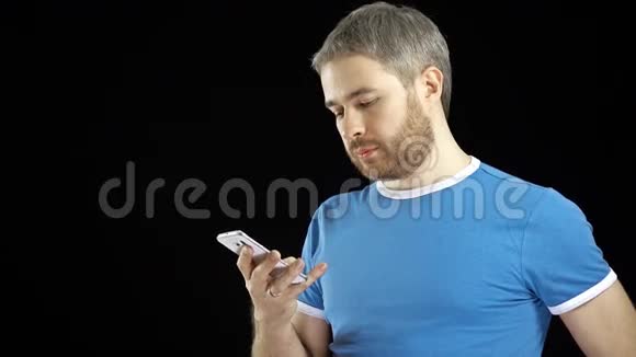 穿蓝色t恤的帅哥在黑色背景下点击他的智能手机触摸屏4K视频视频的预览图