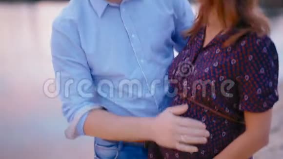 英俊的丈夫拥抱和亲吻他怀孕的妻子在日落湖海滩视频的预览图