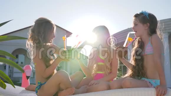 有钱的孩子在日光浴床上手里拿着椰子鸡尾酒在户外快乐的童年被宠坏的孩子带着彩色鸡尾酒视频的预览图