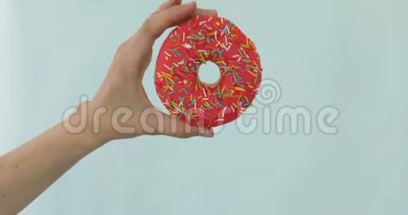 女用手拿着蓝色背景的粉红色甜甜圈视频的预览图