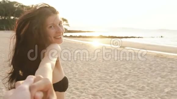 慢动作跟着我拍摄一个穿比基尼的年轻女孩在日落时在海滩上奔跑牵着男人的手视频的预览图