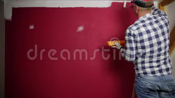 家庭改善戴红帽子的人用油漆滚筒和油漆刷给房间着色视频的预览图