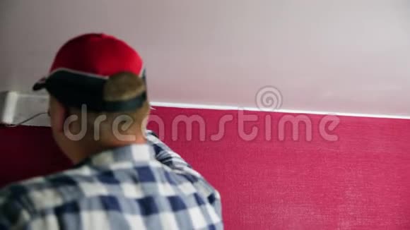 家庭改善戴红帽子的人用油漆滚筒和油漆刷给房间着色视频的预览图
