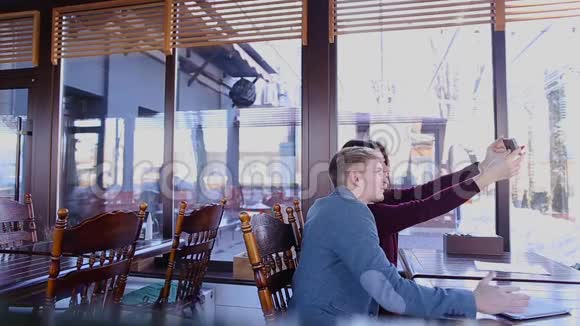 年轻夫妇在咖啡馆的智能手机前摄像头上拍自拍照片视频的预览图