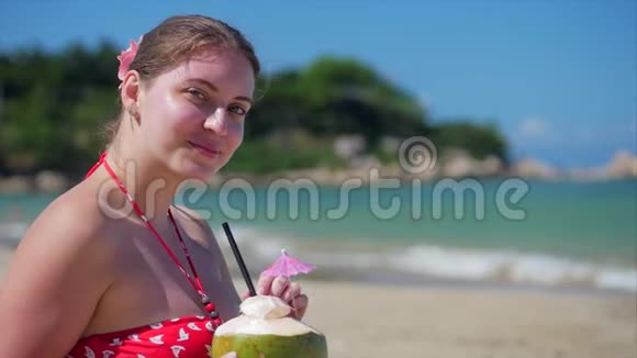 一位欧洲美丽可爱的黑发年轻女子或一位开朗的女孩的特写肖像在阳光下喝一杯椰子视频的预览图