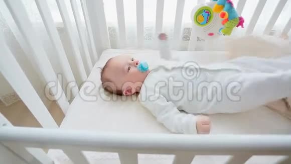3个月大的男孩躺在白色木制婴儿床上玩具旋转木马视频的预览图