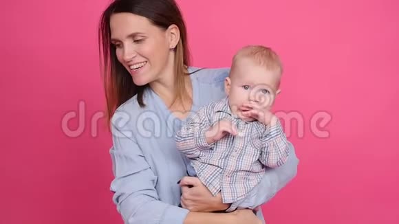 年轻快乐的女人在粉红色的背景上拥抱她的小儿子视频的预览图