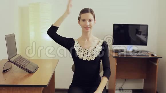 漂亮的女孩在办公室里用右手推着她的头练习健身视频的预览图