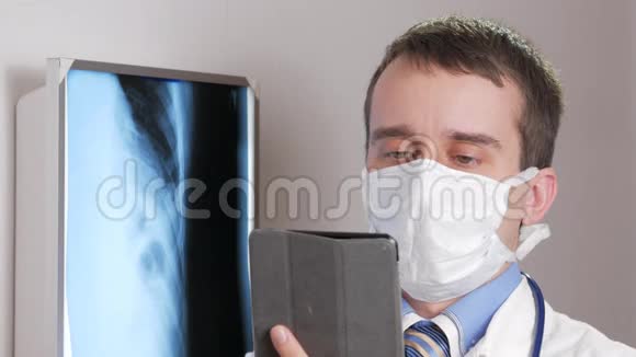 一位戴面膜的年轻医生在诊所里使用平板电脑一名男子记录了一名病人x线的结果视频的预览图