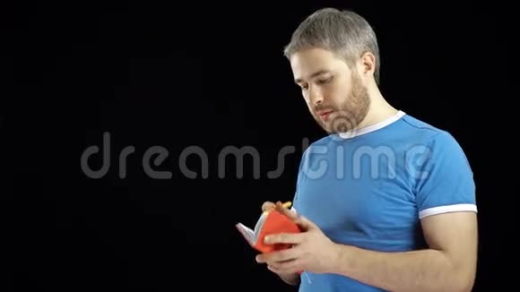 穿蓝色t恤的帅哥在他的红色笔记本上写字备忘录搜索或联系概念黑色背景4K视频视频的预览图
