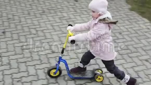 慢动作穿着温暖的帽子和夹克的小女孩在户外骑迷你滑板车视频的预览图
