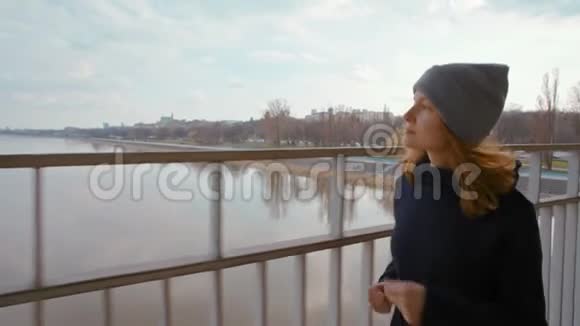 在城市的一条河上的桥上奔跑的运动型美女的慢动作视频的预览图