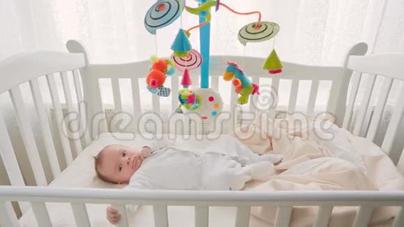 3个月大的可爱宝宝躺在床上看着玩具旋转木马视频的预览图