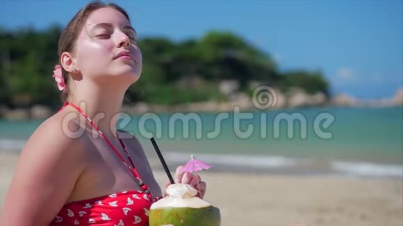 一位欧洲美丽可爱的黑发年轻女子或一位开朗的女孩的特写肖像在阳光下喝一杯椰子视频的预览图