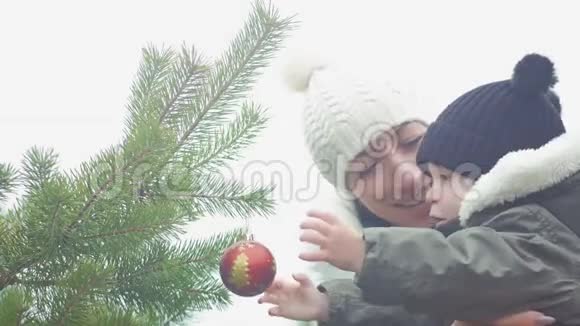 一位年轻的母亲和小儿子在户外装饰圣诞树像一个充满爱的家庭理念快乐视频的预览图