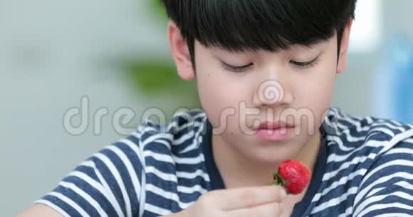 可爱的亚洲男孩带着微笑在家吃草莓视频的预览图