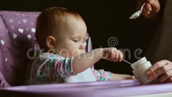 可爱的婴儿坐在高椅上在灰色背景下喂食视频的预览图