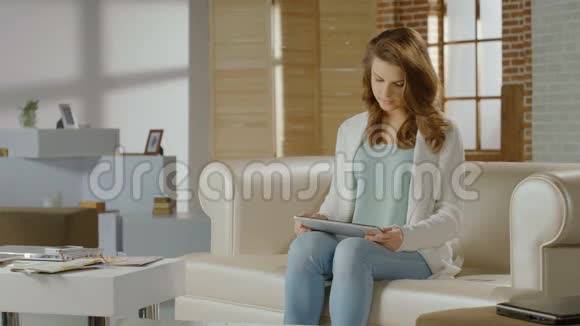 年轻女士在家看平板电脑上的视频视频的预览图