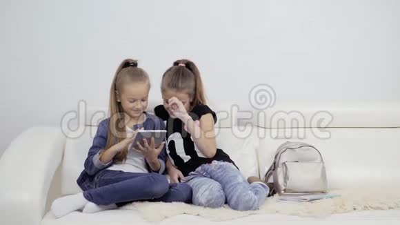 带平板电脑的女孩室内两个女朋友的肖像两个少女看着笔记本电脑平板电脑视频的预览图