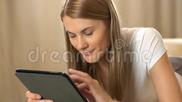 美丽迷人的年轻女子穿着白色t恤一台平板电脑躺在沙发上浏览互联网及视频的预览图