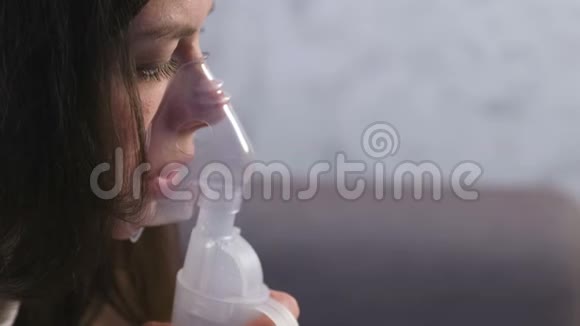 使用雾化器和吸入器进行治疗年轻女性通过吸入面罩吸入特写面部侧视视频的预览图