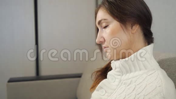 年轻女子穿着温暖的毛衣坐在沙发上在家喝茶视频的预览图