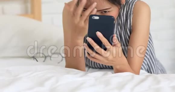 可爱的亚洲女人带着手机在床上聊天发短信视频的预览图