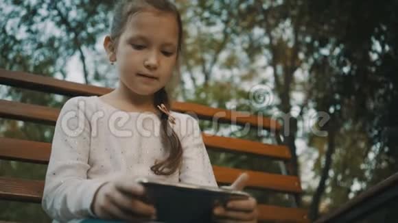 女学生坐在公园的木凳上使用智能手机视频的预览图