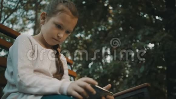 女学生坐在公园的木凳上使用智能手机视频的预览图