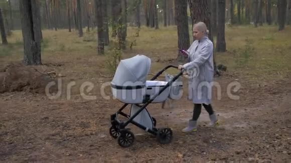 年轻可爱的妈妈带着婴儿车在公园散步用你的手机视频的预览图