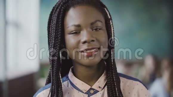 年轻的非洲女人看着相机在忙碌的现代办公室微笑的肖像工作中的成功员工视频的预览图
