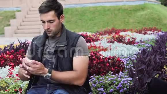 坐在公园里的漂亮聪明的黑发意大利男人期待着见面打电话天气好放松视频的预览图