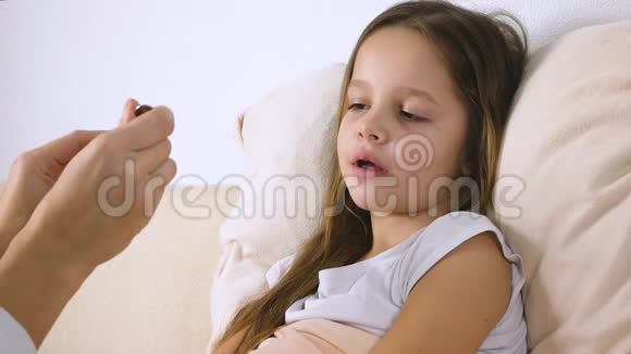 母亲或医生在床上给生病的女儿喂药视频的预览图